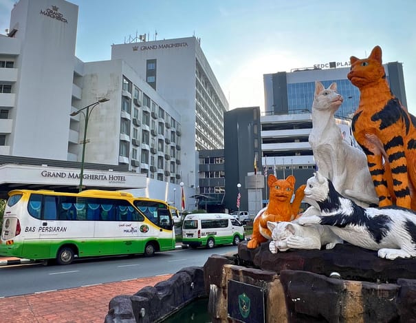 The Kuching Cat Statue at dusk, with an INSAR coach passing the Grand Margherita
